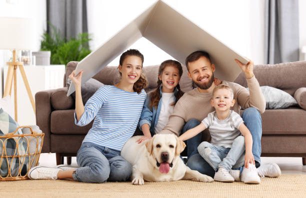 A family enjoys time together on the floor with their dog, playing and laughing around a colorful cardboard house, representing the joy and peace of mind that comes with professional pest control.