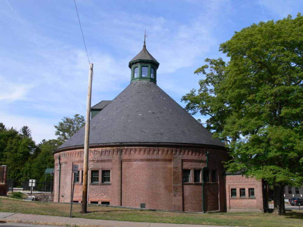 The Attleborough Falls Gasholder Building in North Attleborough, MA, featuring a round structure with a conical slate roof and cupola-like top.