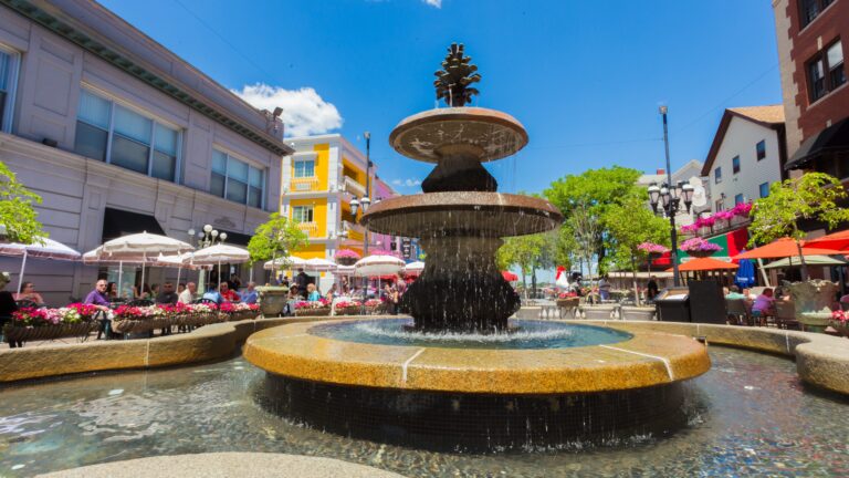 Fountain on Federal Hill near Venda in Providence, RI, surrounded by colorful flowers, outdoor seating, and lively storefronts, capturing the neighborhood’s charm.