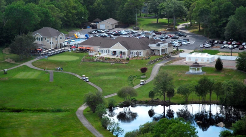 Scenic view of Hillside Country Club’s lush golf course in Rehoboth, MA, with rolling green hills, a picturesque clubhouse, and a clear blue sky.