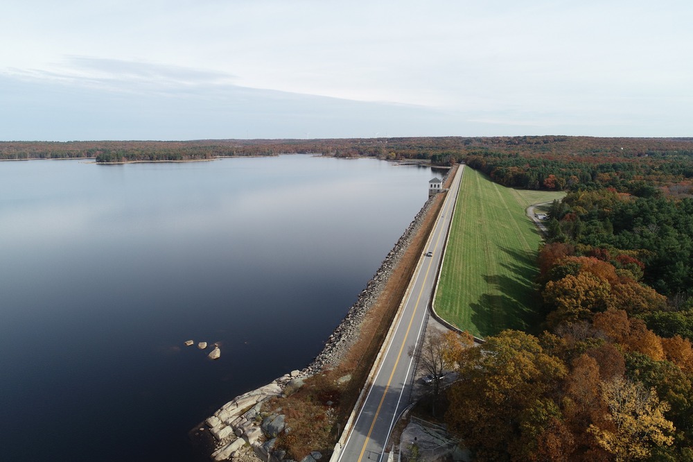 A scenic road leading to the dam at Scituate Reservoir, surrounded by lush greenery and calm waters.