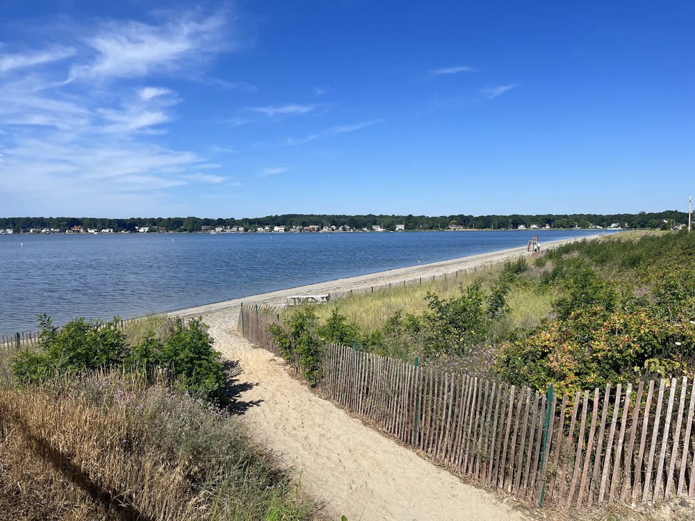 Scenic view of Swansea Town Beach in Swansea, MA, featuring a sandy shoreline, gentle waves, and a clear blue sky.